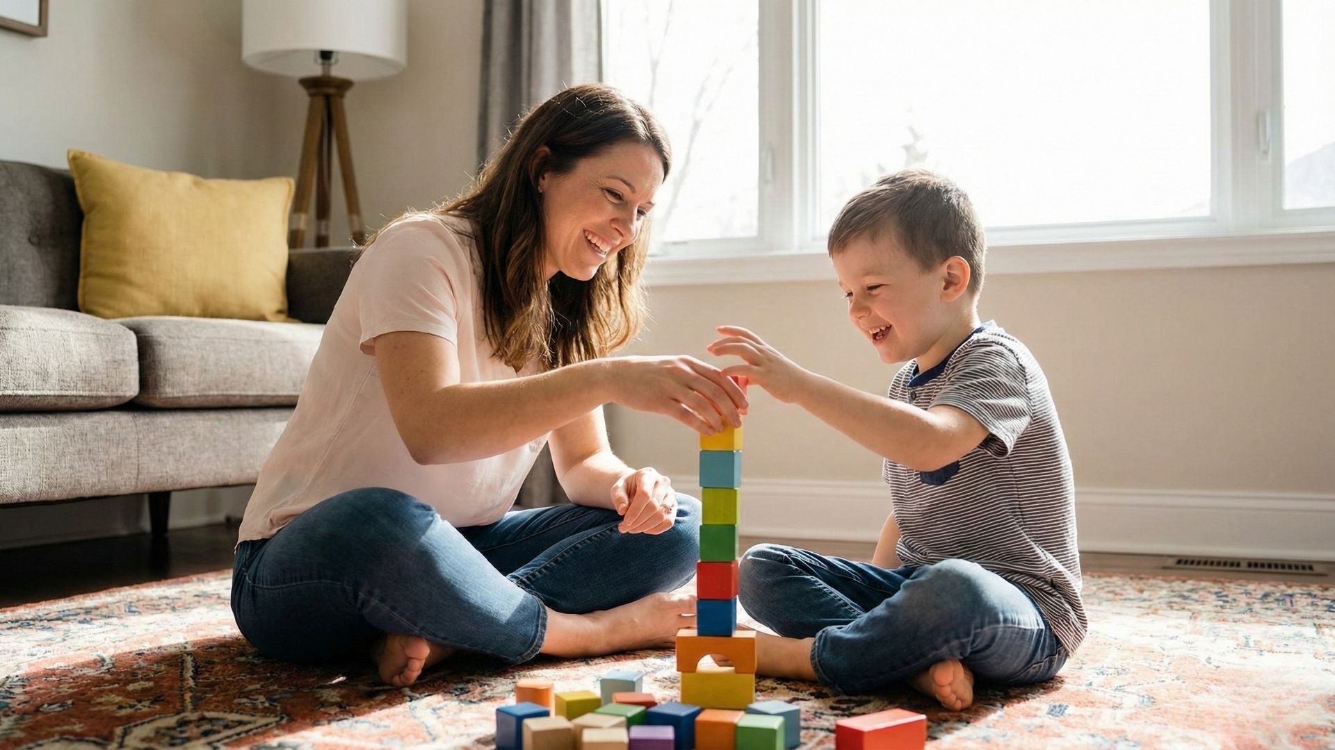 therapist and young boy happily playing with blocks on a living room rug