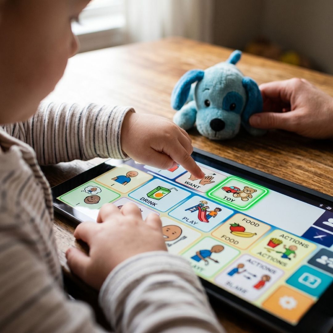 Close-up of a child's hands using a tablet with communication icons to interact with a caregiver.